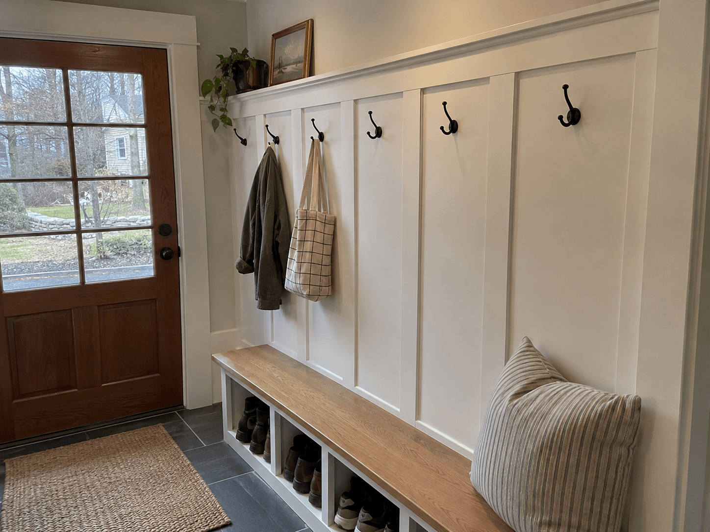 Mudroom entryway with white paneled wall, black hooks, and a wooden bench with shoe cubbies.